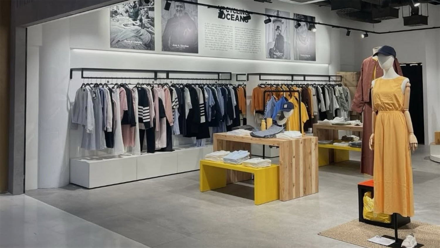 Interior de tienda Ecoalf con ropa expuesta en percheros de madera y maniquíes vestidos con prendas sostenibles.