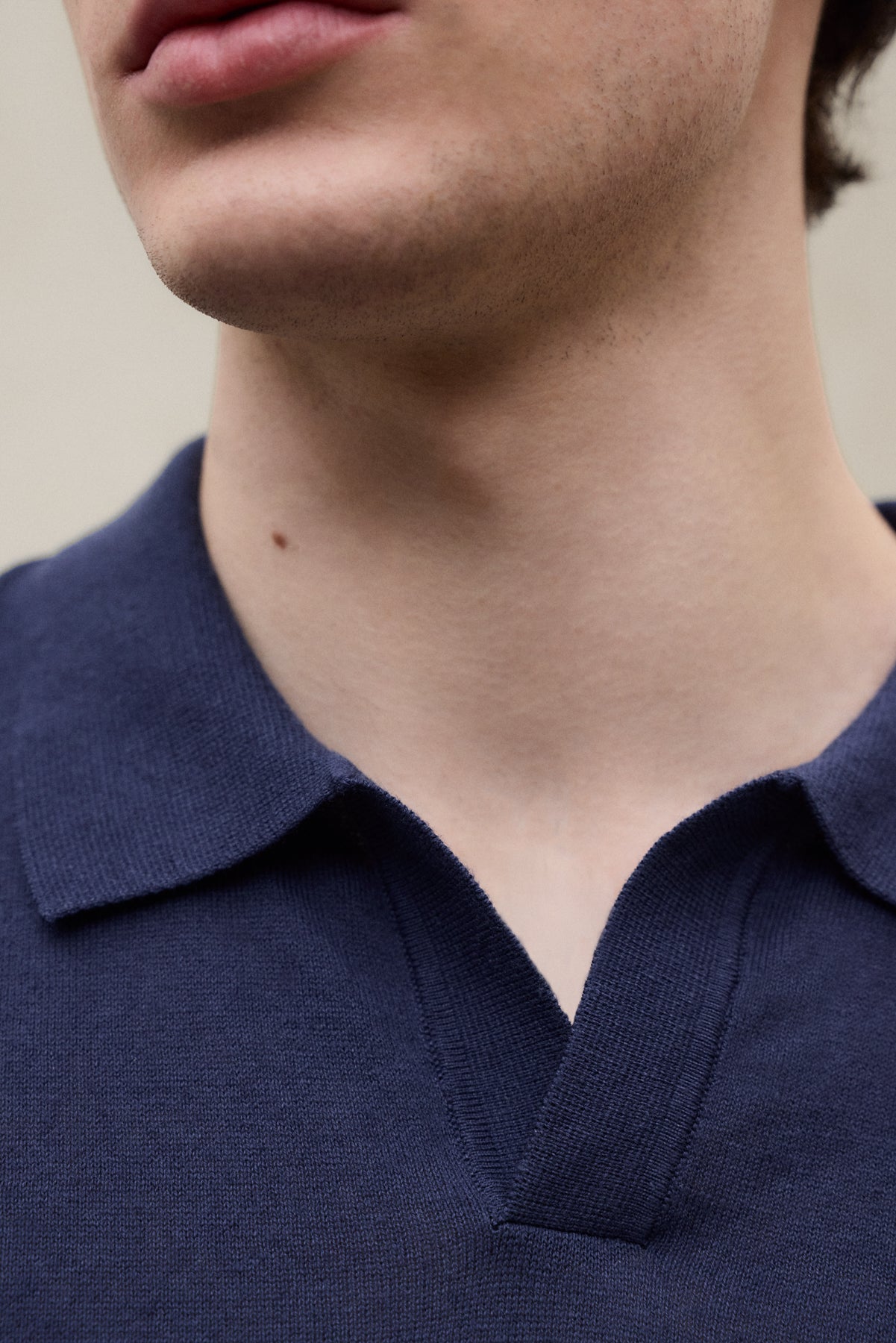 Primer plano de la parte baja del rostro de una persona con una camiseta de Ecoalf azul oscuro de cuello en pico.