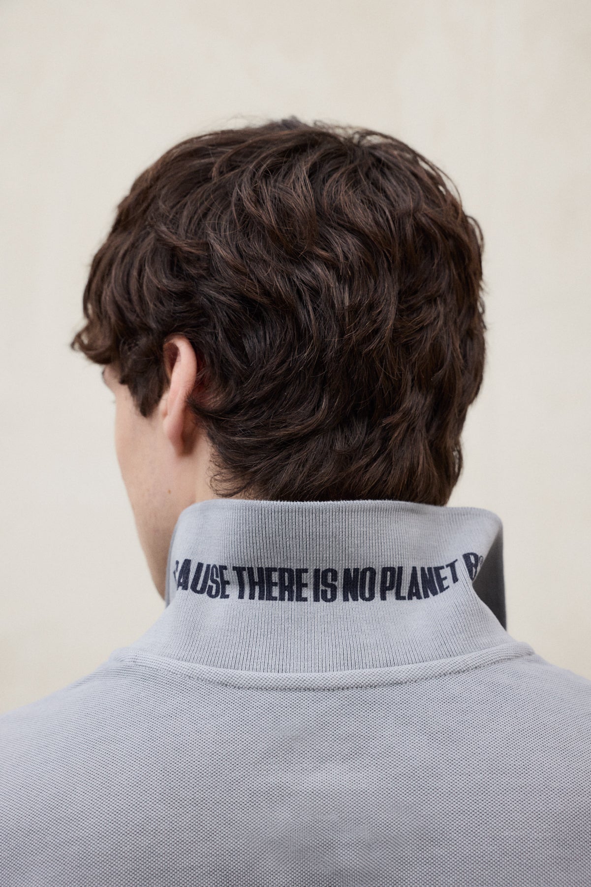 El cuello alto de una chaqueta de Ecoalf gris visto por detrás, con el lema "THERE IS NO PLANET B", sobre fondo claro.