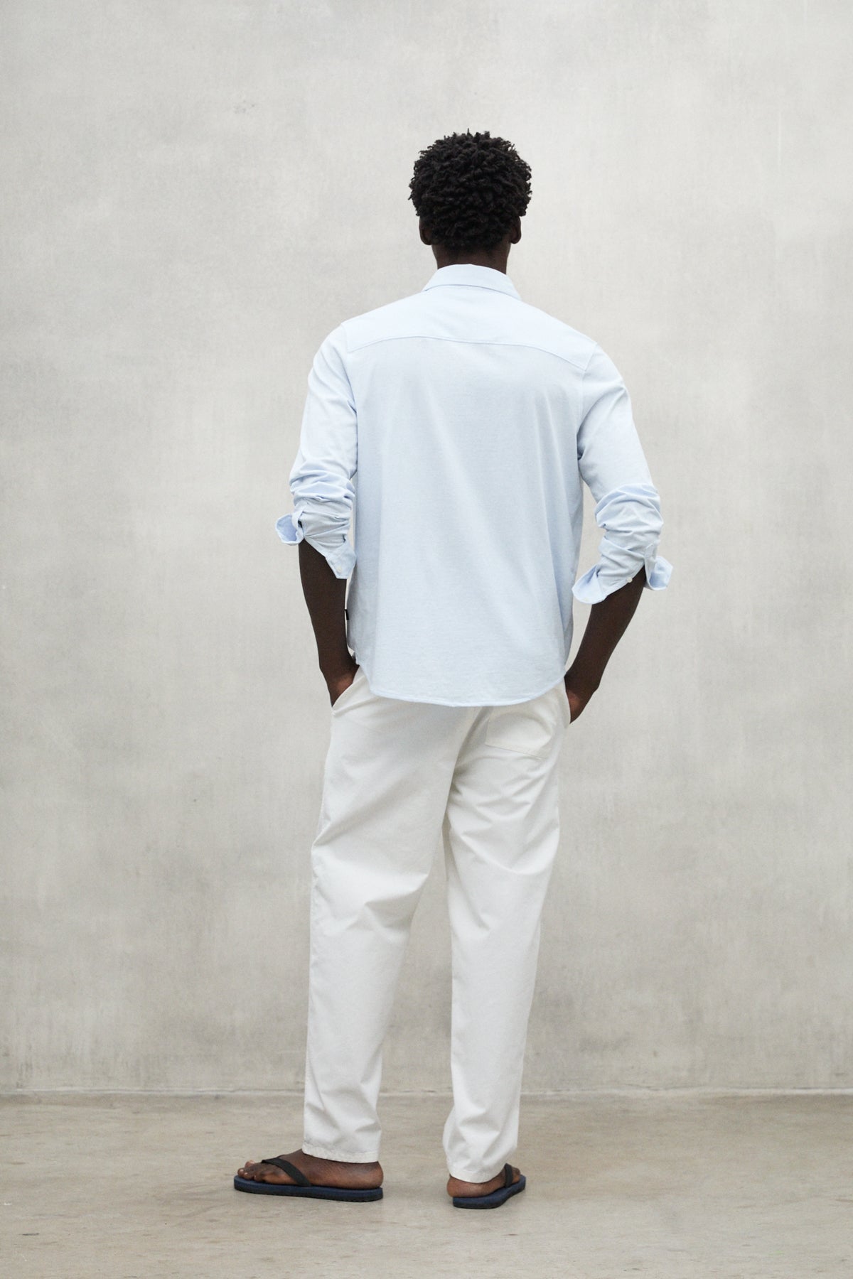 Un hombre de espaldas vistiendo camisa azul claro y pantalón blanco de materiales sostenibles de la firma Ecoalf.