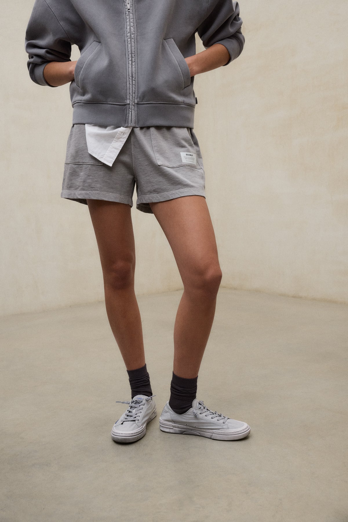 Shorts grises sostenibles de la marca ecoalf.probinados con zapatillas blancas y calcetines oscuros para un estilo casual.